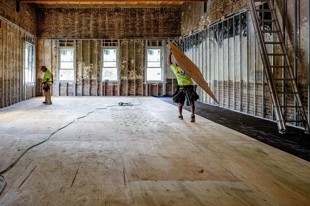 Gutted room with exposed framing and a worker carrying a panel