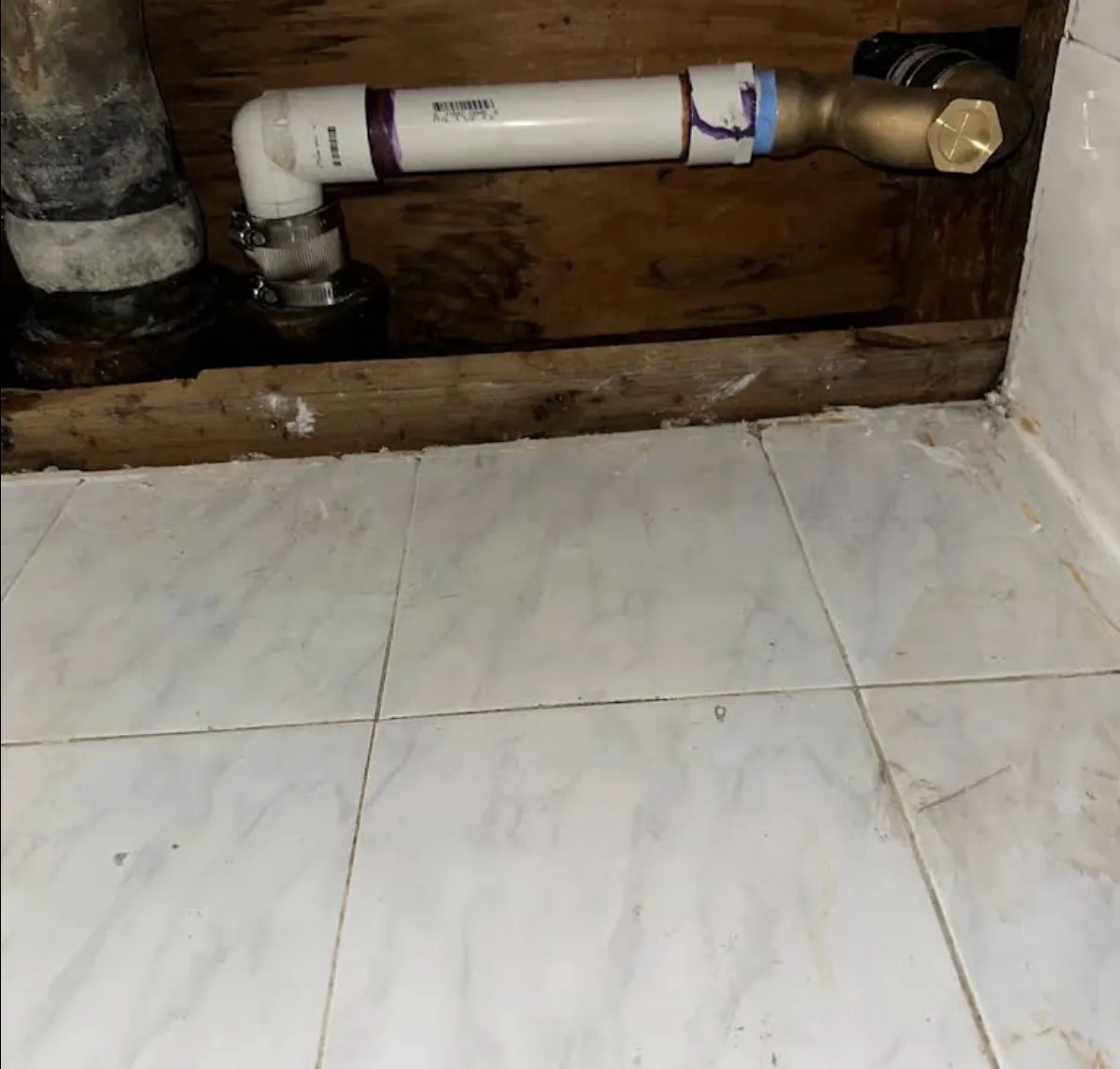 White drain and valve assembly in an opened cabinet base above a tile floor