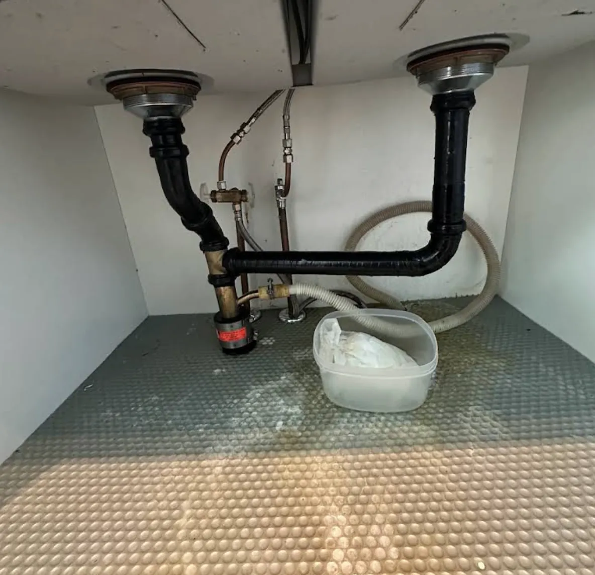 Double kitchen sink drain with black trap pipes and a dishwasher hose