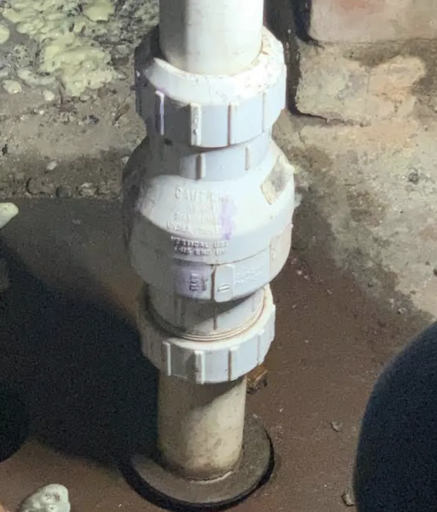 White PVC check valve fitted into a basement drain line