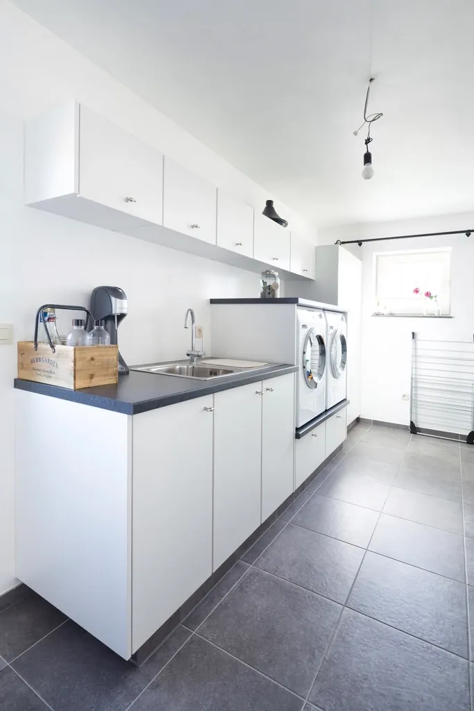 Compact white kitchen and laundry area with dark tile floor